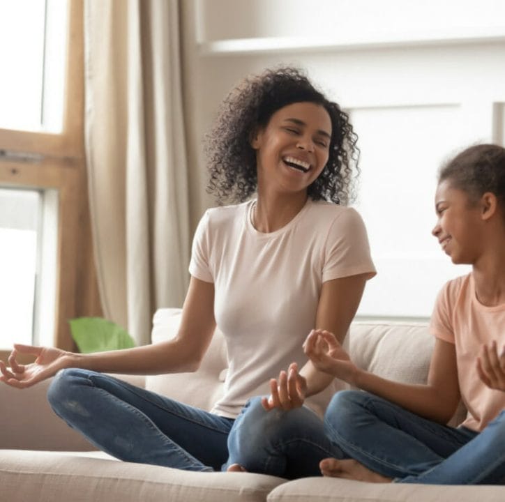 Mom and daughter laughing and doing yoga on sofa